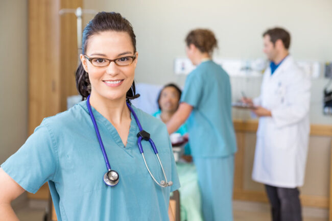 Nurse Smiling Against Patient And Medical Team In Hospital