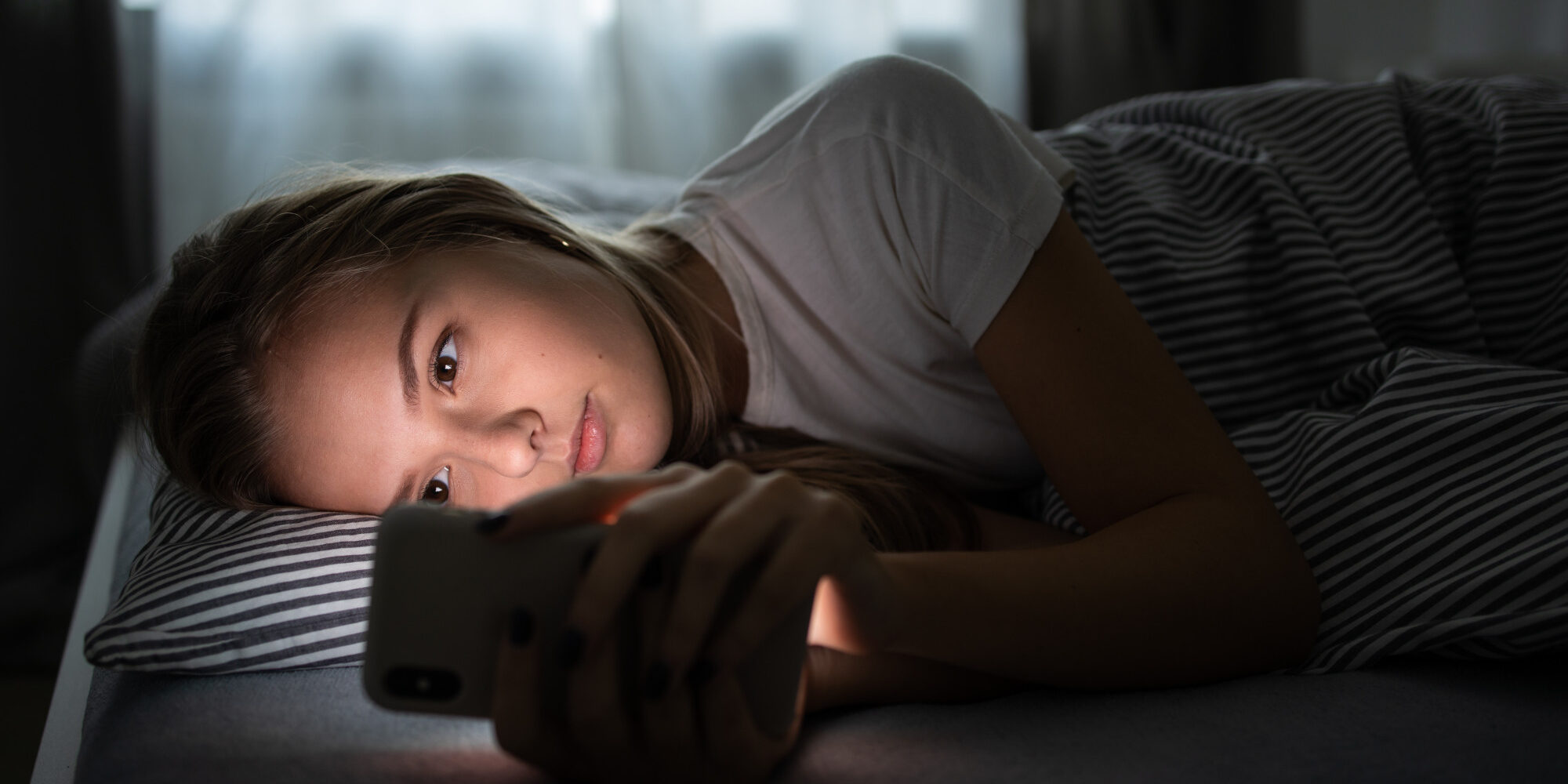 Pretty, young woman sleeping in her bed with her cell phone clos