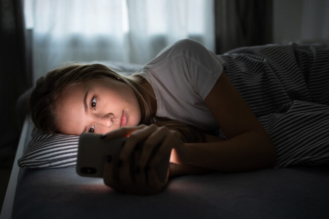 Pretty, young woman sleeping in her bed with her cell phone clos