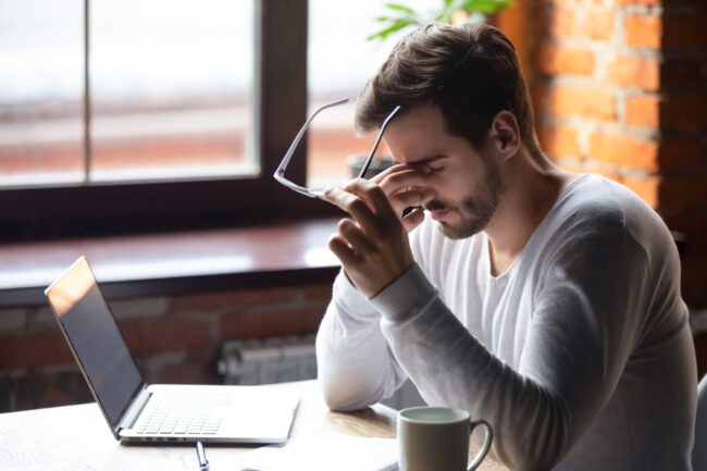 Upset man massaging nose bridge, taking off glasses, feeling eye strain